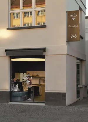 Exterior of Naše maso butcher shop with storefront window and staff inside.