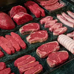Raw beef and pork cuts, steaks, chops and sausages displayed on a butcher’s marble counter.