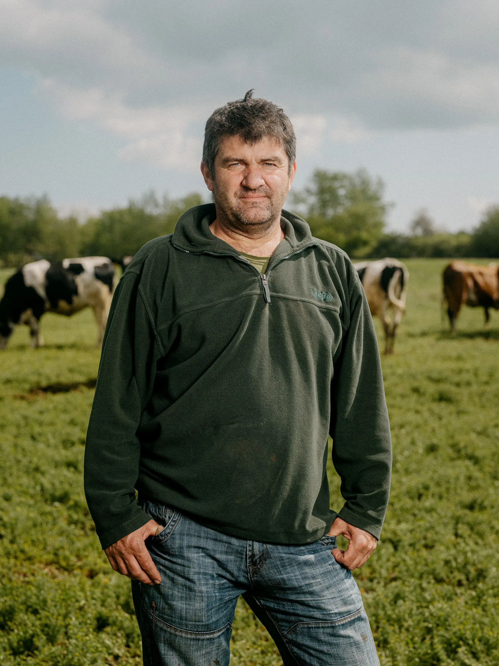 Farmer standing in a pasture with cows in the background.